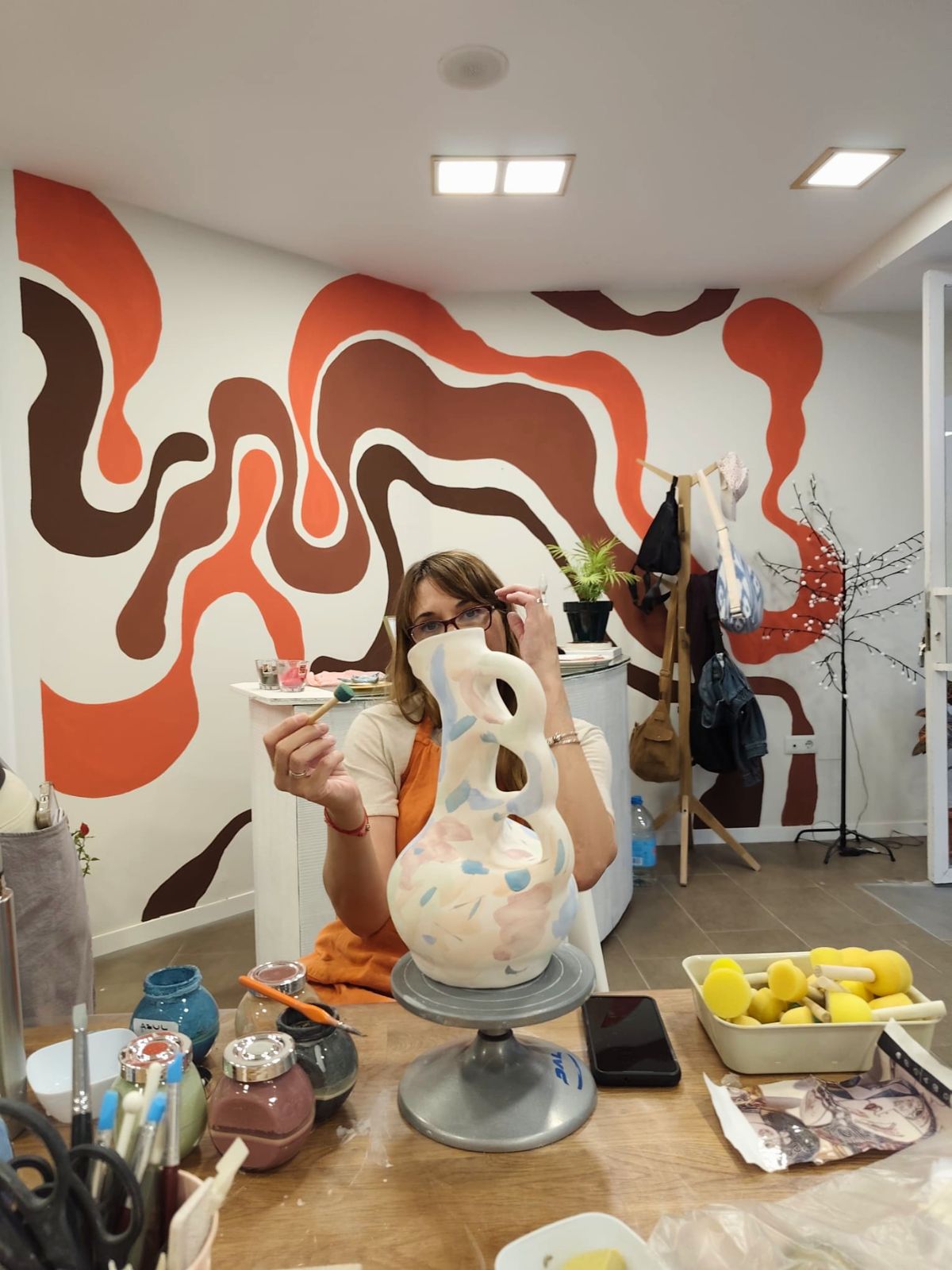Alumna pintando una pieza escultórica frente al mural de colores del taller de cerámica en Málaga