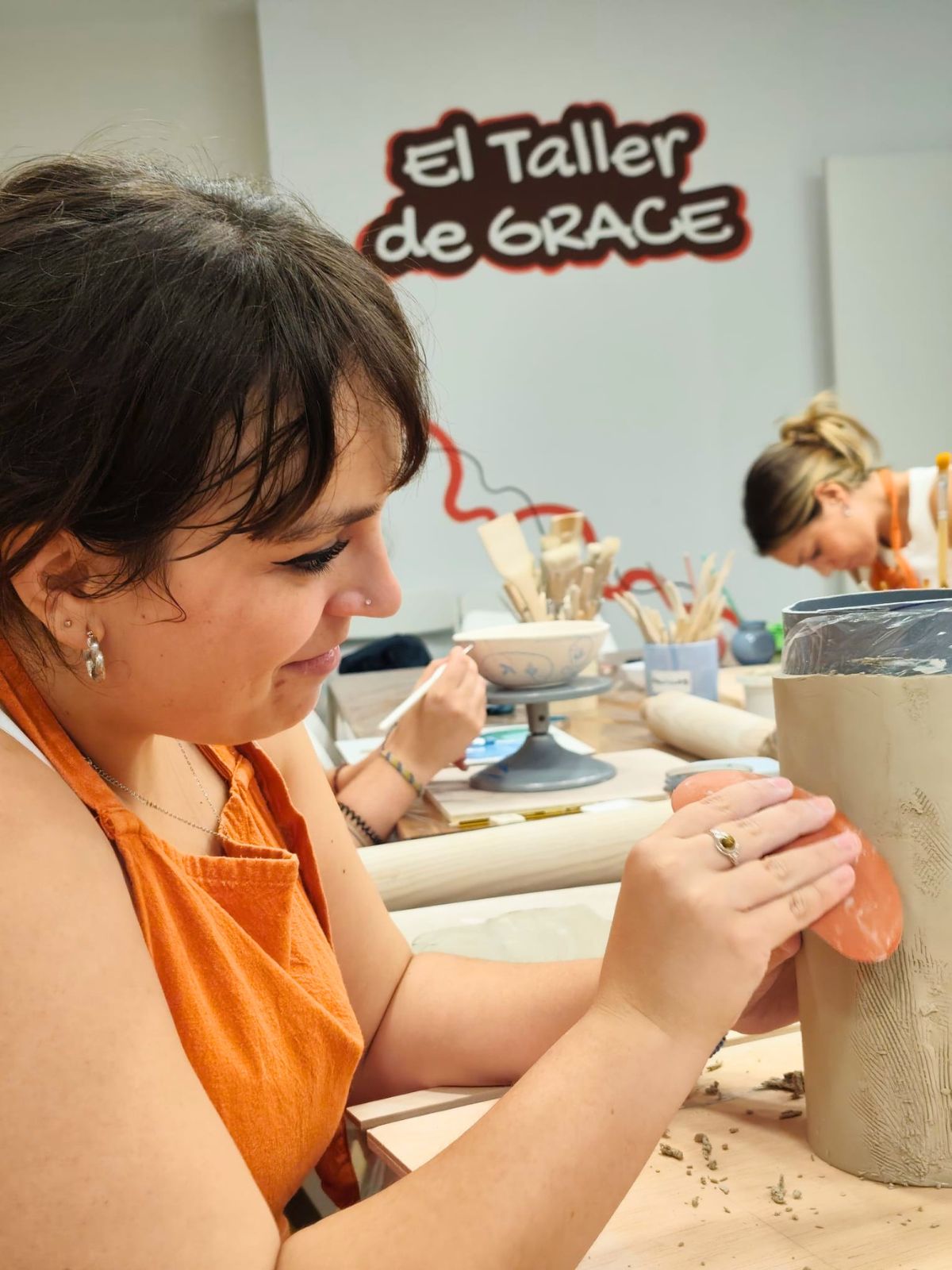 Alumna sonriendo mientras trabaja una pieza grande de cerámica artesanal