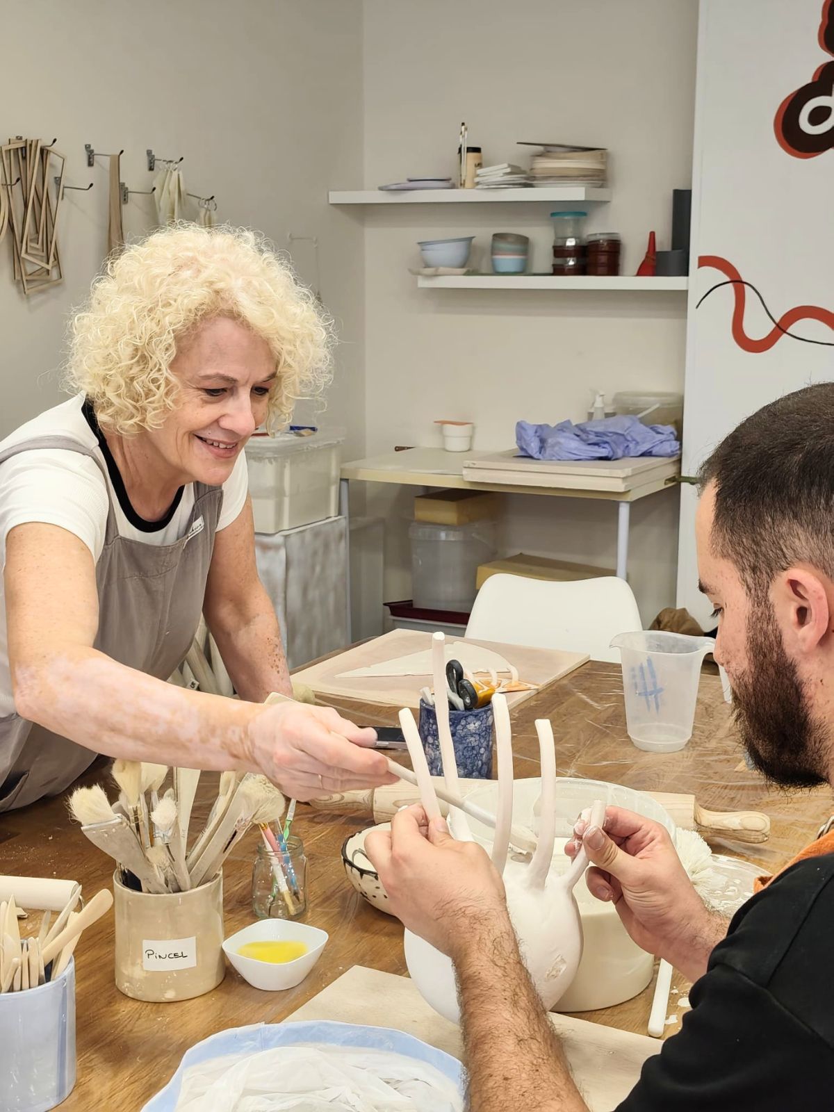 Grace, profesora de cerámica, asistiendo sonriente a un alumno durante el taller en Málaga